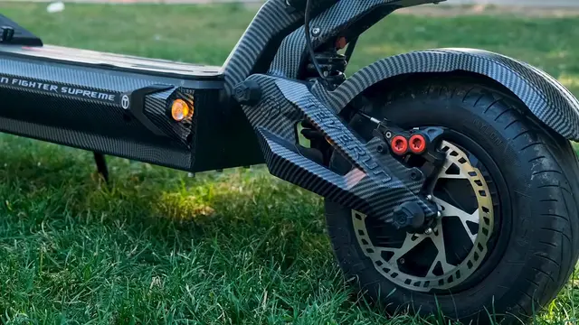 Karbon kaplamalı Teverun 7260R V4'ün Teverun yazılı arka salıncak kolu, kırmızı kaliperi, delikli diski ve turuncu yan ışığı; çimen üzerinde