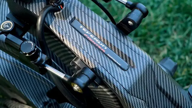 Karbon kaplamalı Teverun 7260R V4'te TEVERUN FIGHTER SUPREME yazılı plaka ve damping ayarlı amortisör yakın plan; arkada çimen