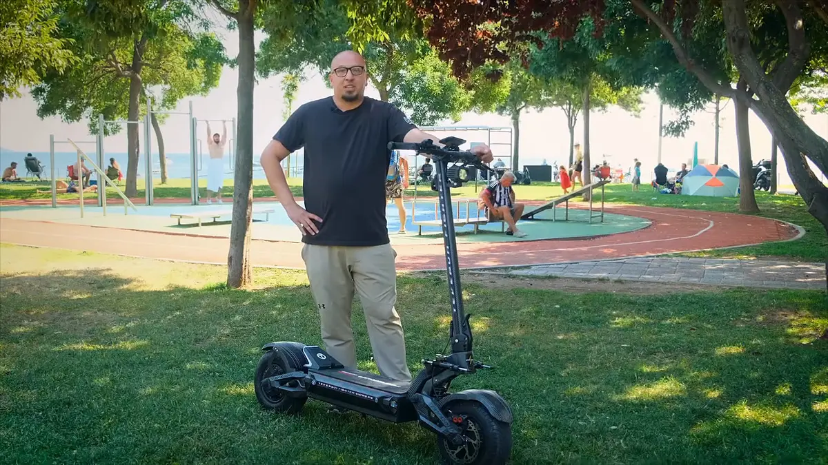Koyu tişörtlü, gözlüklü bir adam ağaçlı sahil parkında karbon kaplamalı Teverun 7260R V4'ün yanında duruyor
