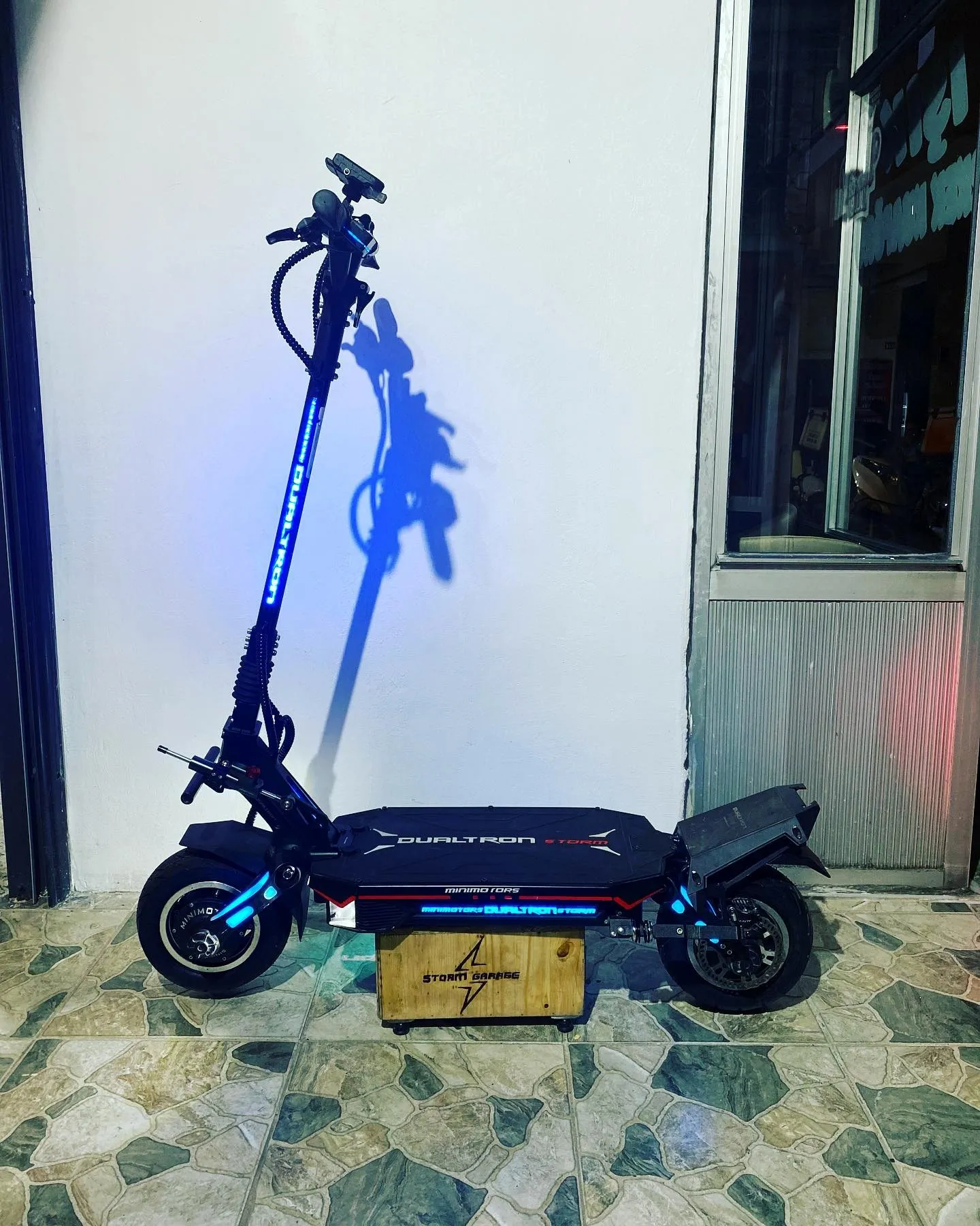 Gidon ve gövde LED’leri mavi yanan Dualtron Storm Limited, Storm Garage ahşap kasası üzerinde