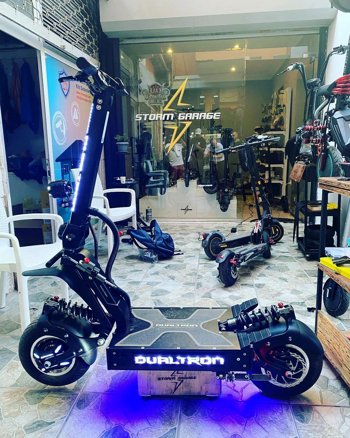 Mavi alt ışıklı Dualtron X2, Storm Garage ahşap kasası üzerinde; arkada dükkânın logolu vitrini