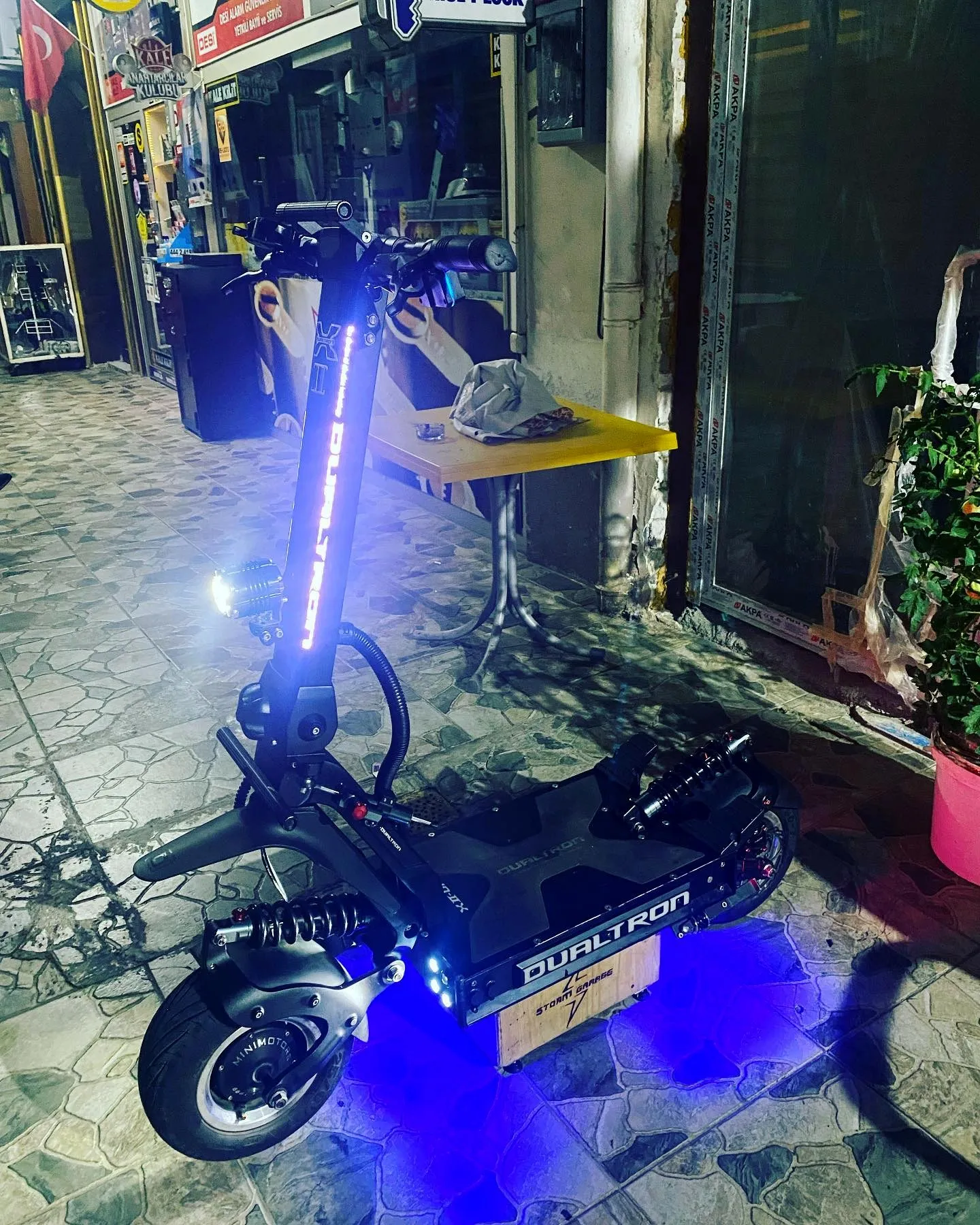 Gece eski dükkânın önünde, Storm Garage kasası üzerinde mavi alt ve gidon LED'leri yanan Dualtron X2
