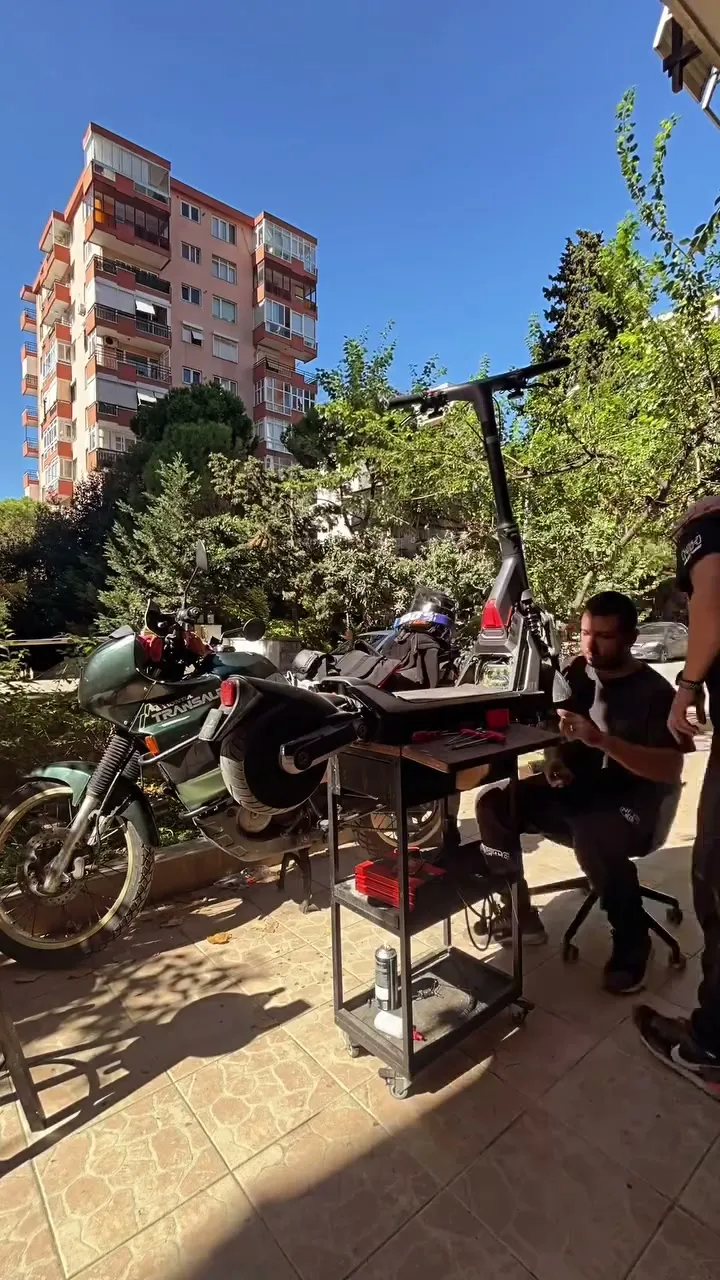 Güneşli bir günde dükkân önünde, servis arabasının başında çalışan teknisyenler