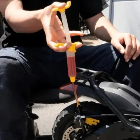Hidrolik fren hava alma işlemi: teknisyen şırıngayla scooter'ın fren kaliperine yağ basıyor