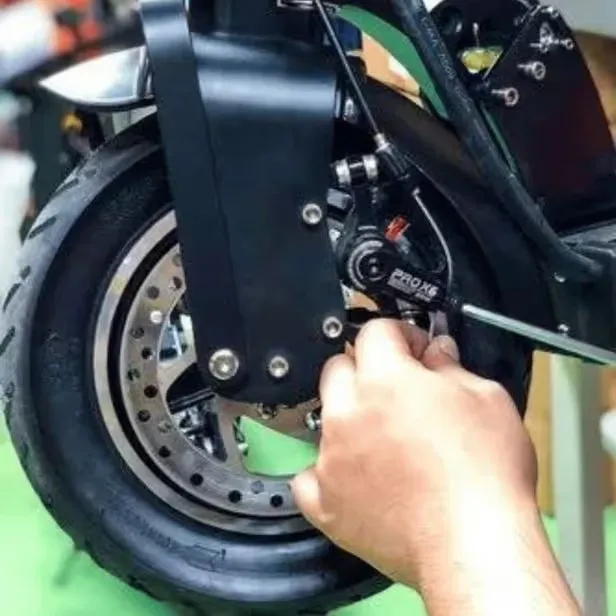 Teknisyen, elektrikli scooter’ın ön tekerindeki disk fren kaliperini el aletiyle ayarlıyor