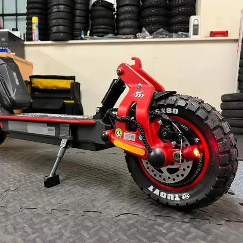 Kırmızı salıncak kollu, Tuovt arazi lastikli elektrikli scooter'ın arka tekeri; arkada raflarda istiflenmiş lastikler